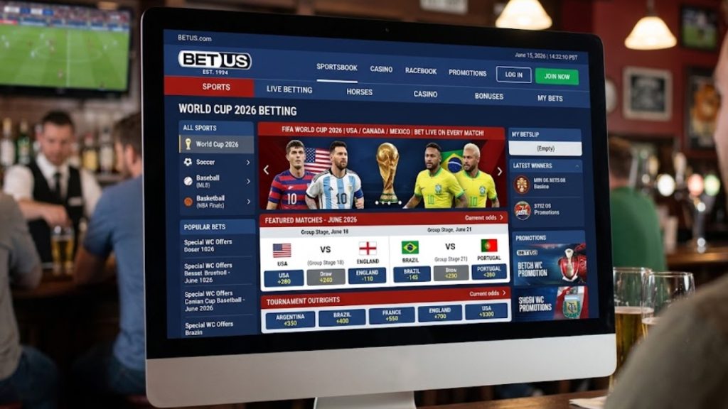 A BetUS review image showing a desktop computer screen displaying the main sportsbook homepage and live World Cup betting markets inside a lively bar environment.