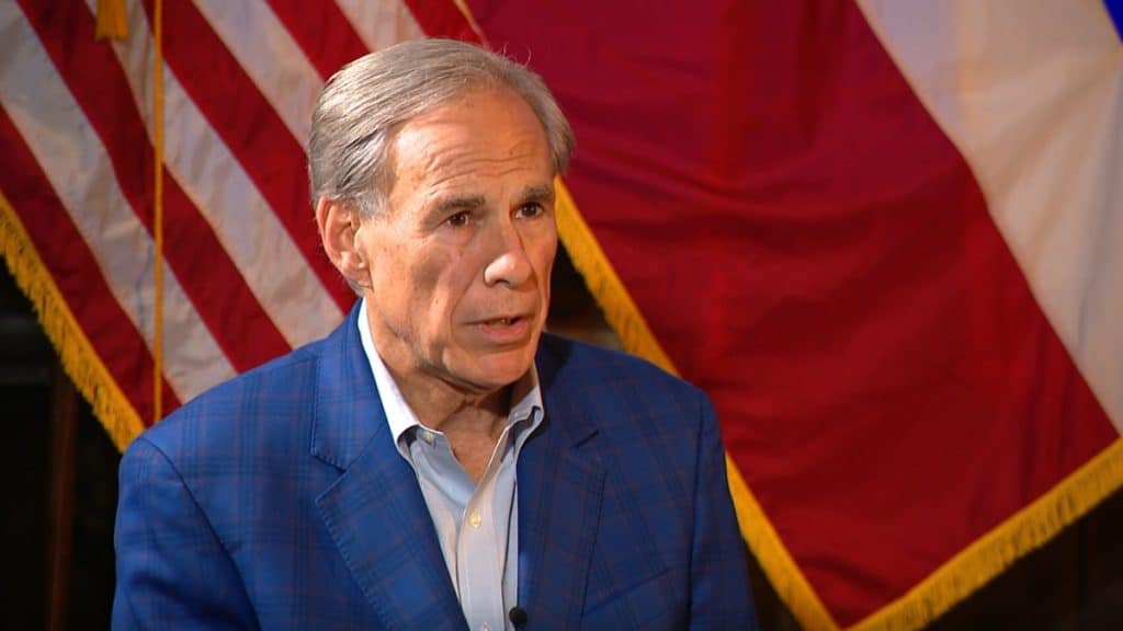 A medium shot of Governor Greg Abbott speaking in front of the Texas and United States flags. The image captures a formal address likely concerning the legislative decisions and executive stance on the future of texas sports betting and gambling expansion.