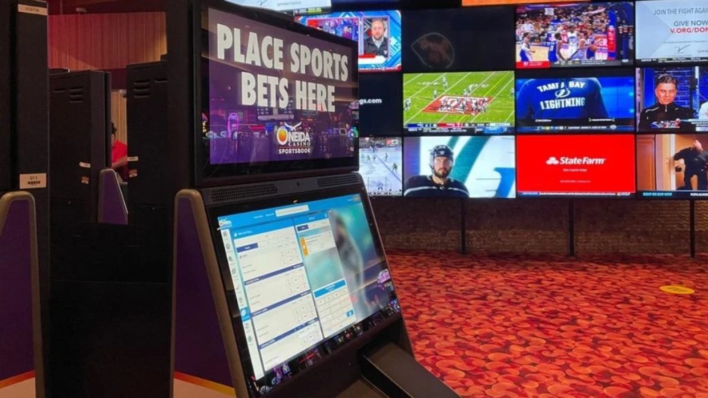 An indoor shot of a retail sportsbook kiosk at Oneida Casino displaying 'Place Sports Bets Here' on screens, highlighting the current in-person wagering options available ahead of the Wisconsin Sports Betting Bill April expansion.