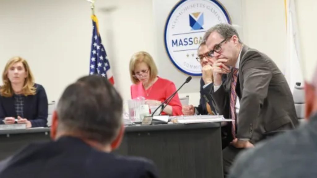 Members of the Massachusetts Gaming Commission seated at a long desk during a formal hearing, overseeing the regulatory implementation and licensing process established by the Massachusetts Sports Betting Bill.
