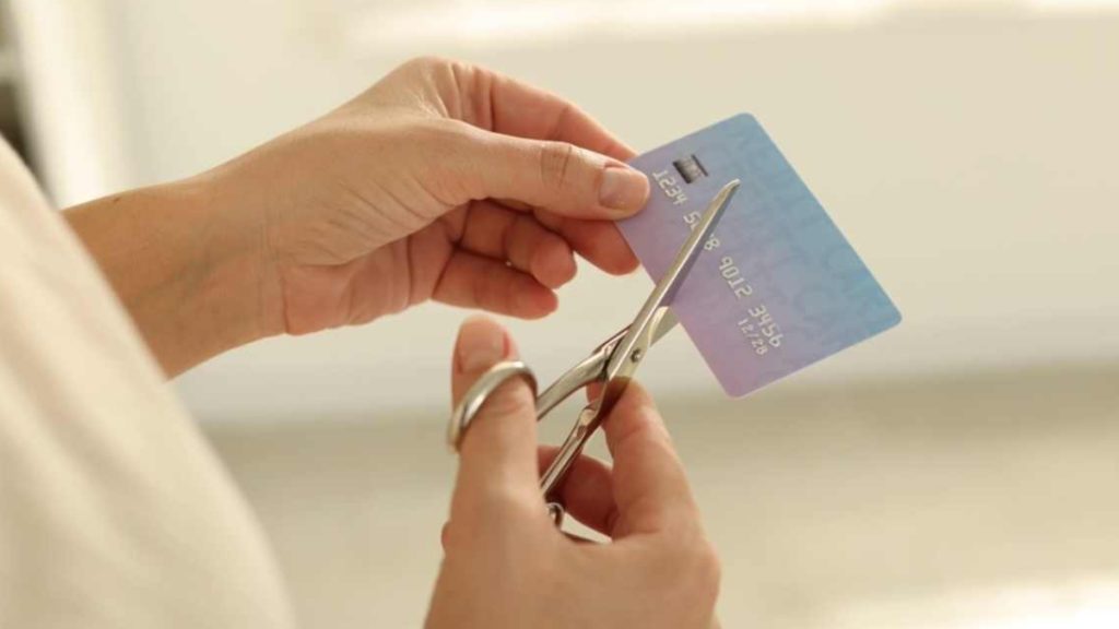 A close-up of a person's hands using scissors to cut a light blue credit card in half. This conceptual image illustrates the potential impact of new regulations aimed at banning any Sports Betting Credit Card from being used for sportsbook deposits.