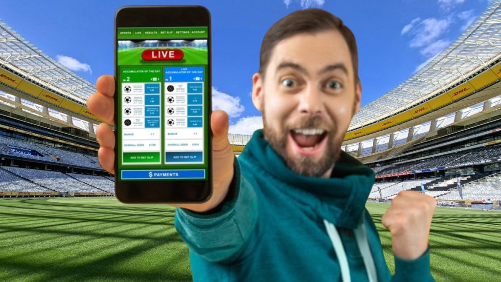 An excited sports fan celebrating in a large stadium while holding up a smartphone showing a live sports betting app interface, representing the upcoming Wisconsin Sports Betting Bill April approval process for online wagering.