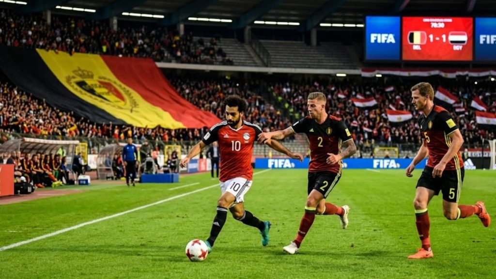 Mohamed Salah dribbling a soccer ball past Belgian defenders Toby Alderweireld and Jan Vertonghen in a packed stadium with a 1-1 scoreboard, showcasing a live moment from Belgium vs Egypt.