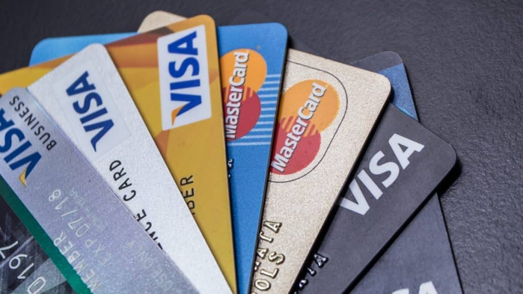 A fan-shaped close-up of various Visa and MasterCard credit cards laid out on a dark surface, illustrating the banking and payment restrictions proposed under Colorado SB26-131.