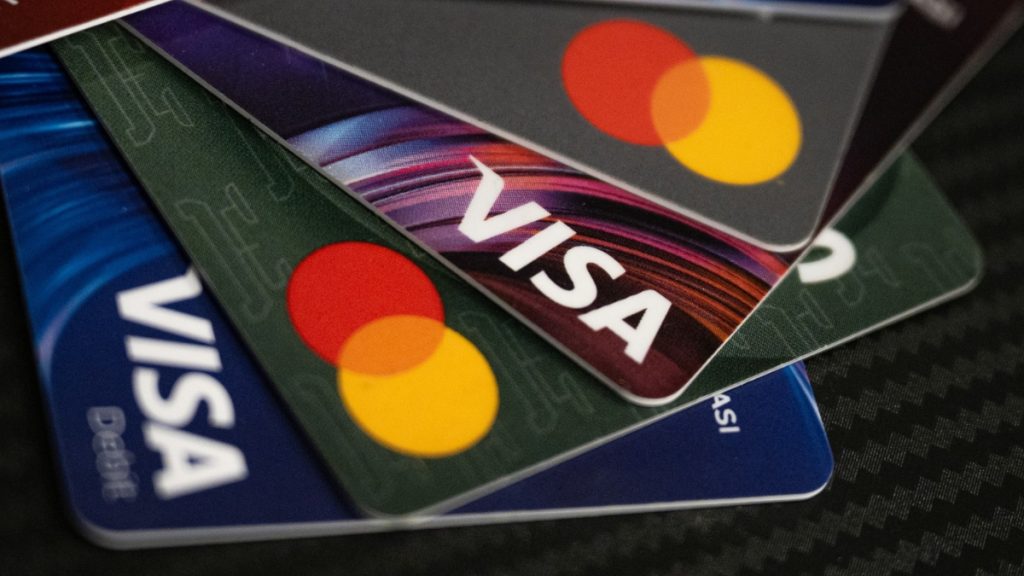 A close-up, fanned-out view of multiple Visa and Mastercard debit and credit cards resting on a dark carbon fiber texture. This visualization emphasizes the proposed payment restrictions being debated as part of the broader Ohio Sports Betting Bill June 2026, including potential limitations on credit card utilization for gaming.