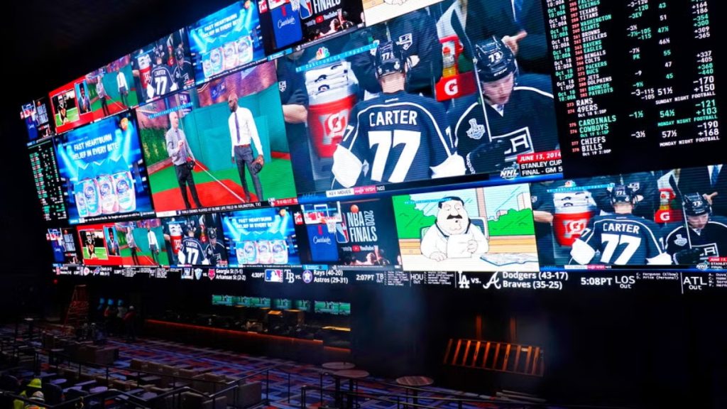 A massive electronic sports betting board inside a casino lounge displaying live odds, point spreads, and upcoming game information next to screens showing live hockey and basketball broadcasts. This image highlights the active retail betting markets operating while the state considers a formal Wisconsin Sports Betting Bill.