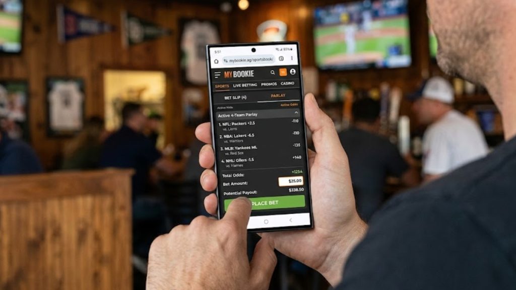 A person holding a smartphone showing the MyBookie mobile interface displaying an active 4-team parlay bet slip for a Bovada vs MyBookie comparison analysis.